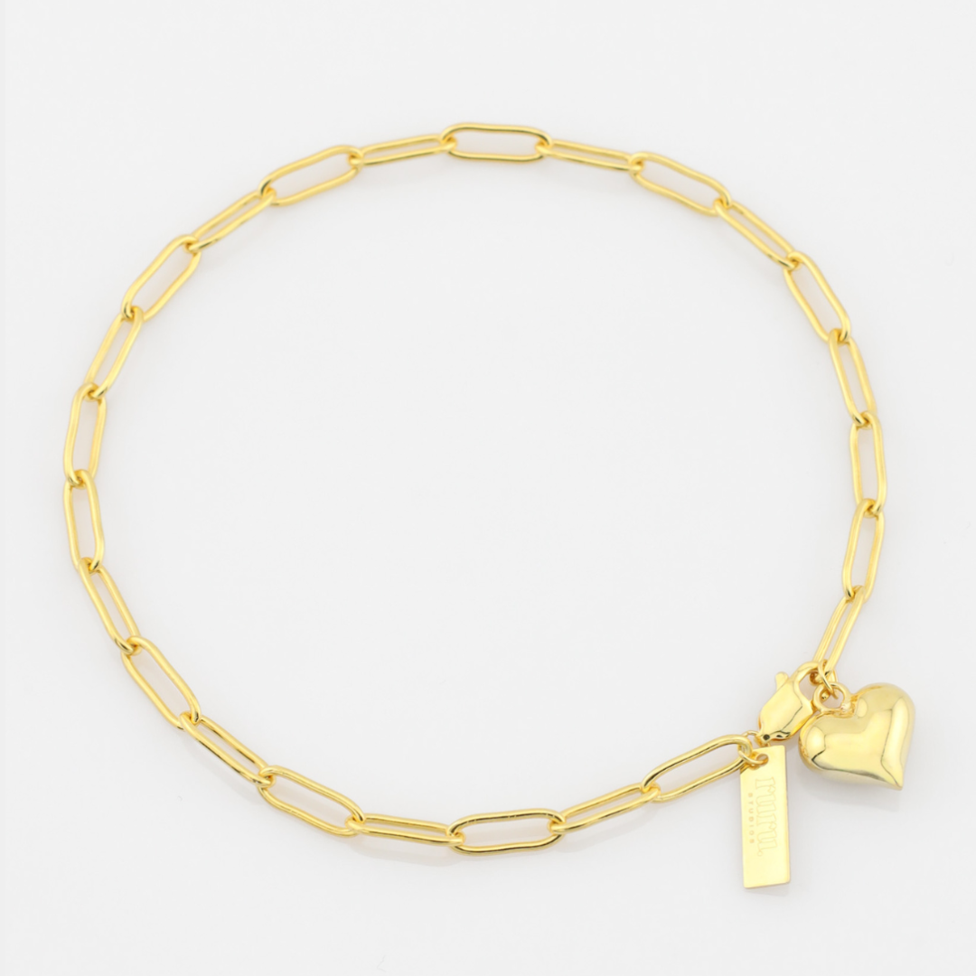 Gold chain bracelet with heart and rectangular tag charm on a white background