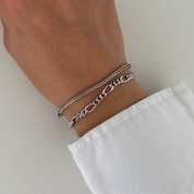 Wrist with two silver bracelets stacked, featuring the chunky chain design of the Autumn bracelet and a delicate textured bracelet, worn with a white shirt.