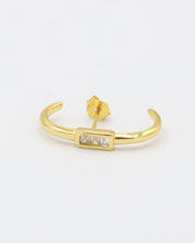 A single gold-colored earring with a small gold charm attached to it, displayed against a white background.