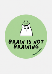 A circular sticker or print with a light green background, featuring a white cartoon cat with a spark of light above its head and the text 'BRAIN IS NOT BRAINING' in black. Small text in the lower right reads 'ruru.