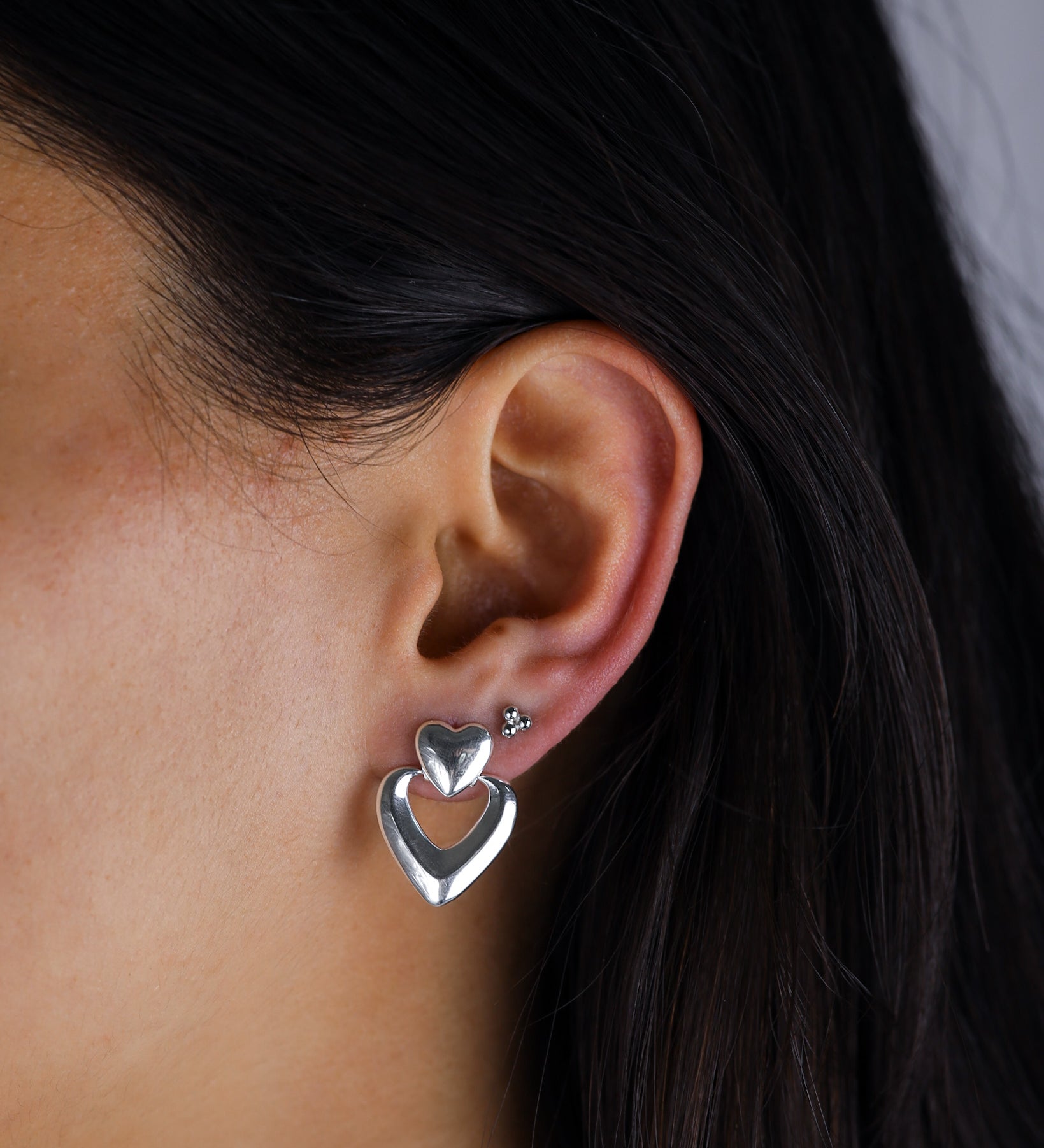 Close-up of an ear wearing a silver heart-shaped earring with a blurred background