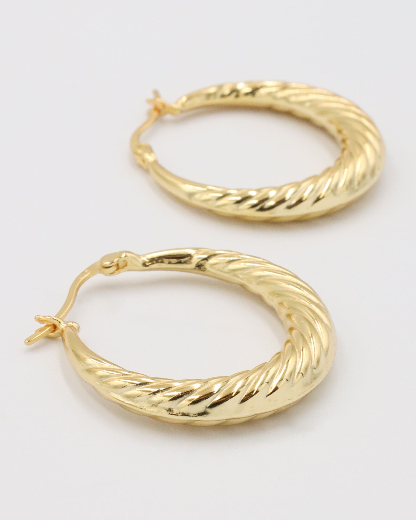 A pair of gold-colored hoop earrings with a latch back clasp on a white background.