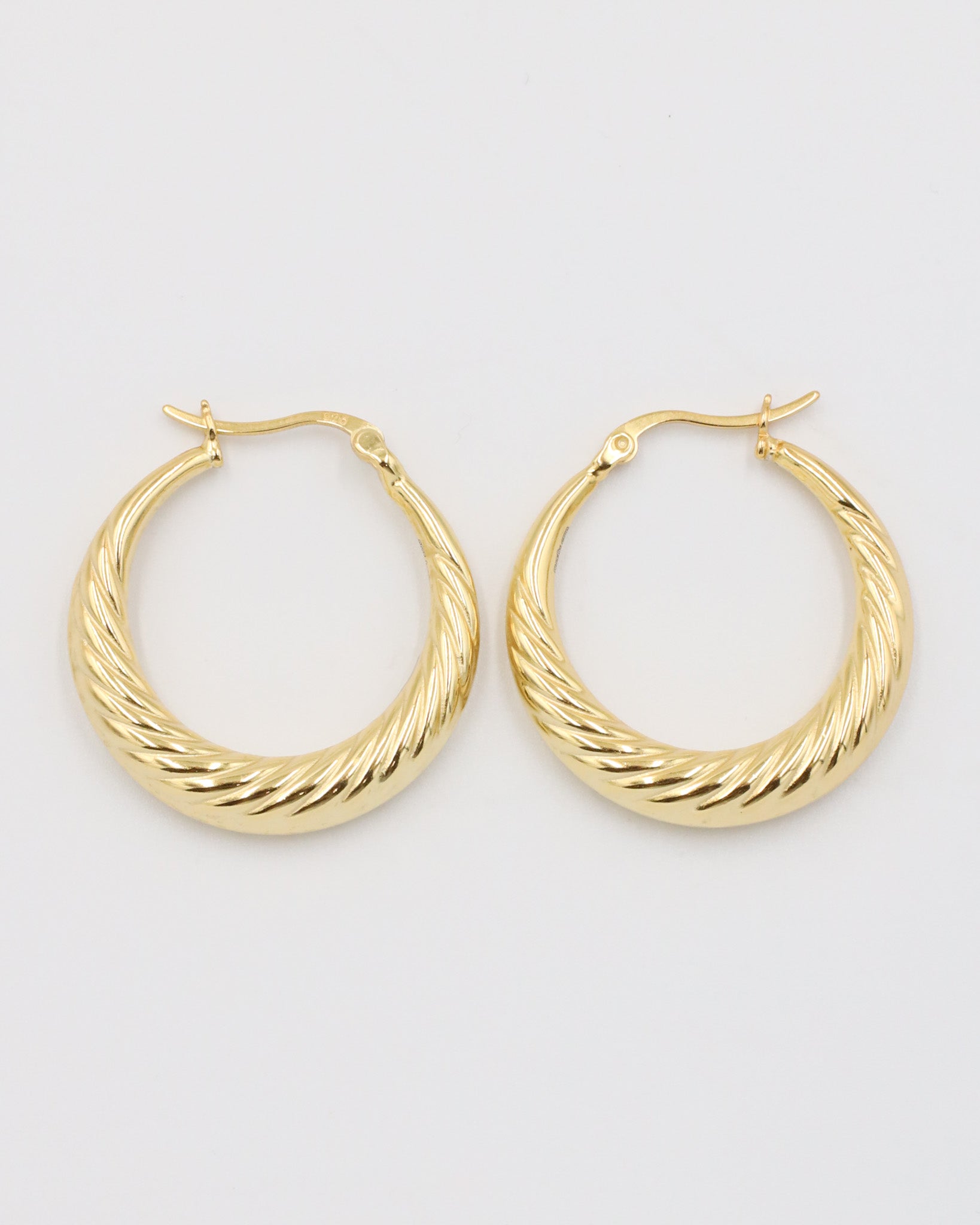 A pair of gold-colored hoop earrings with a latch back clasp on a white background.