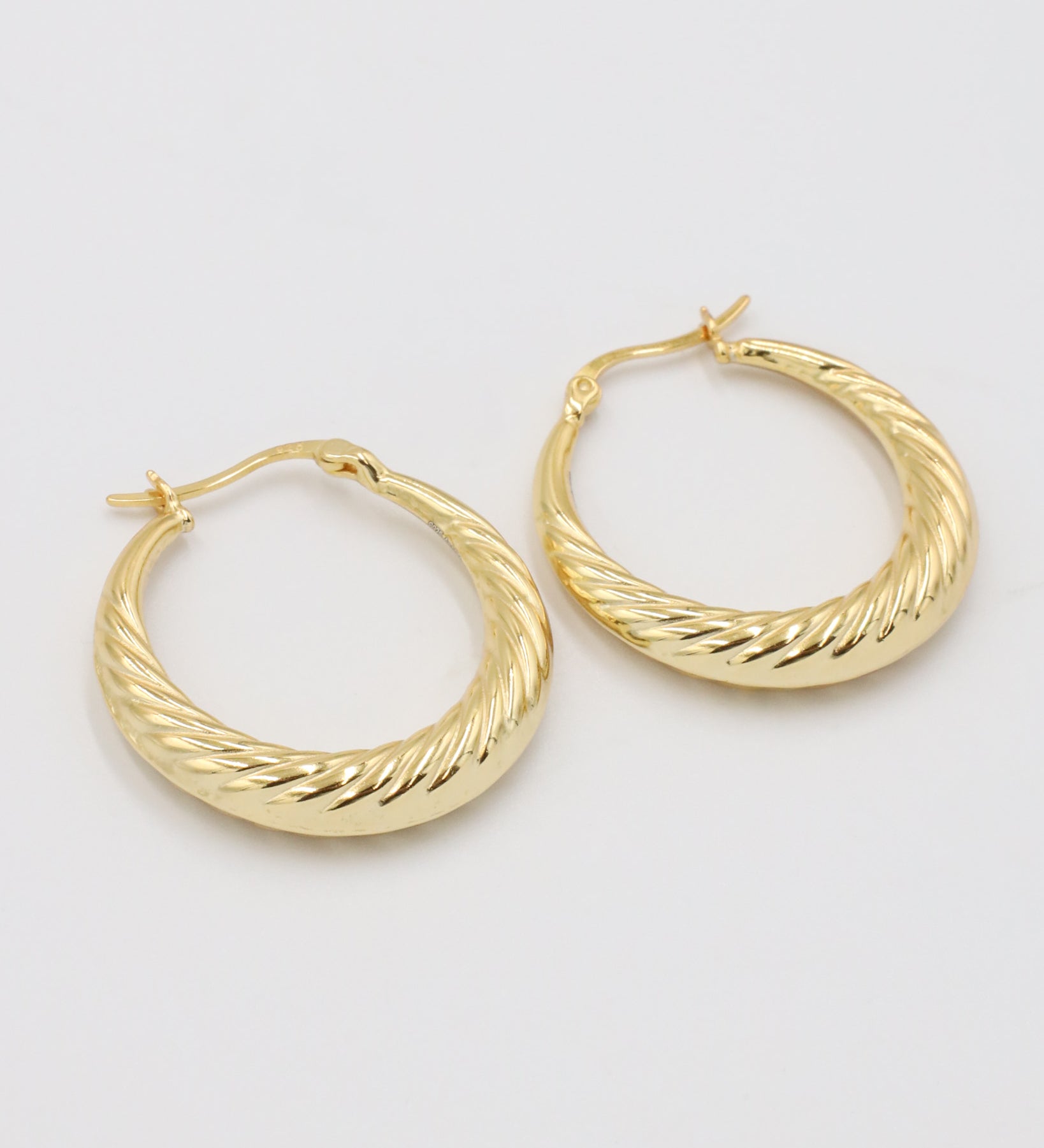 A pair of gold-colored hoop earrings with a latch back clasp on a white background.
