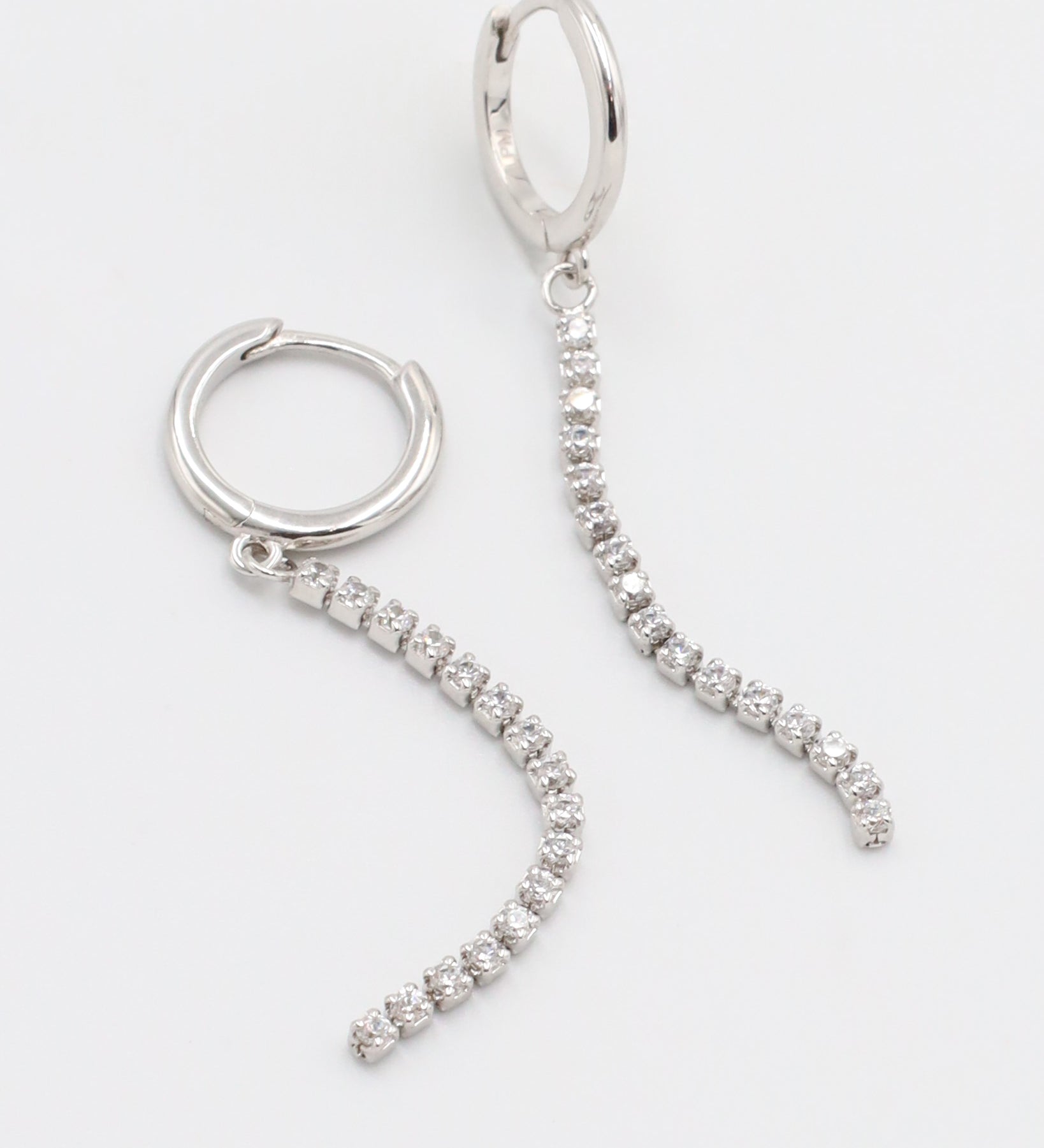 A silver hoop earring with a hinged clasp and small hanging diamonds