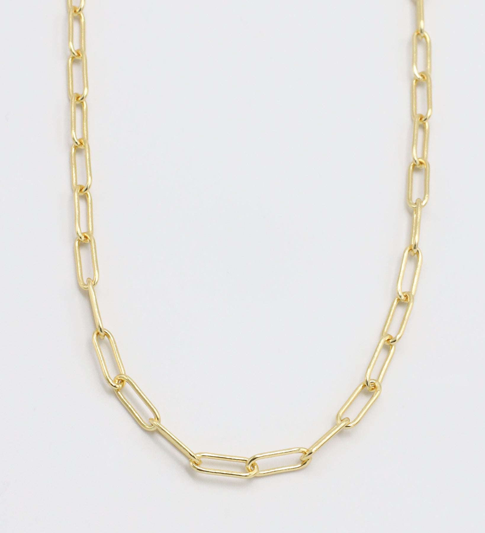 A gold-colored necklace with a chain link design, laid out on a plain background.