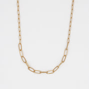 A gold-colored necklace with a chain link pattern laid out on a plain surface.