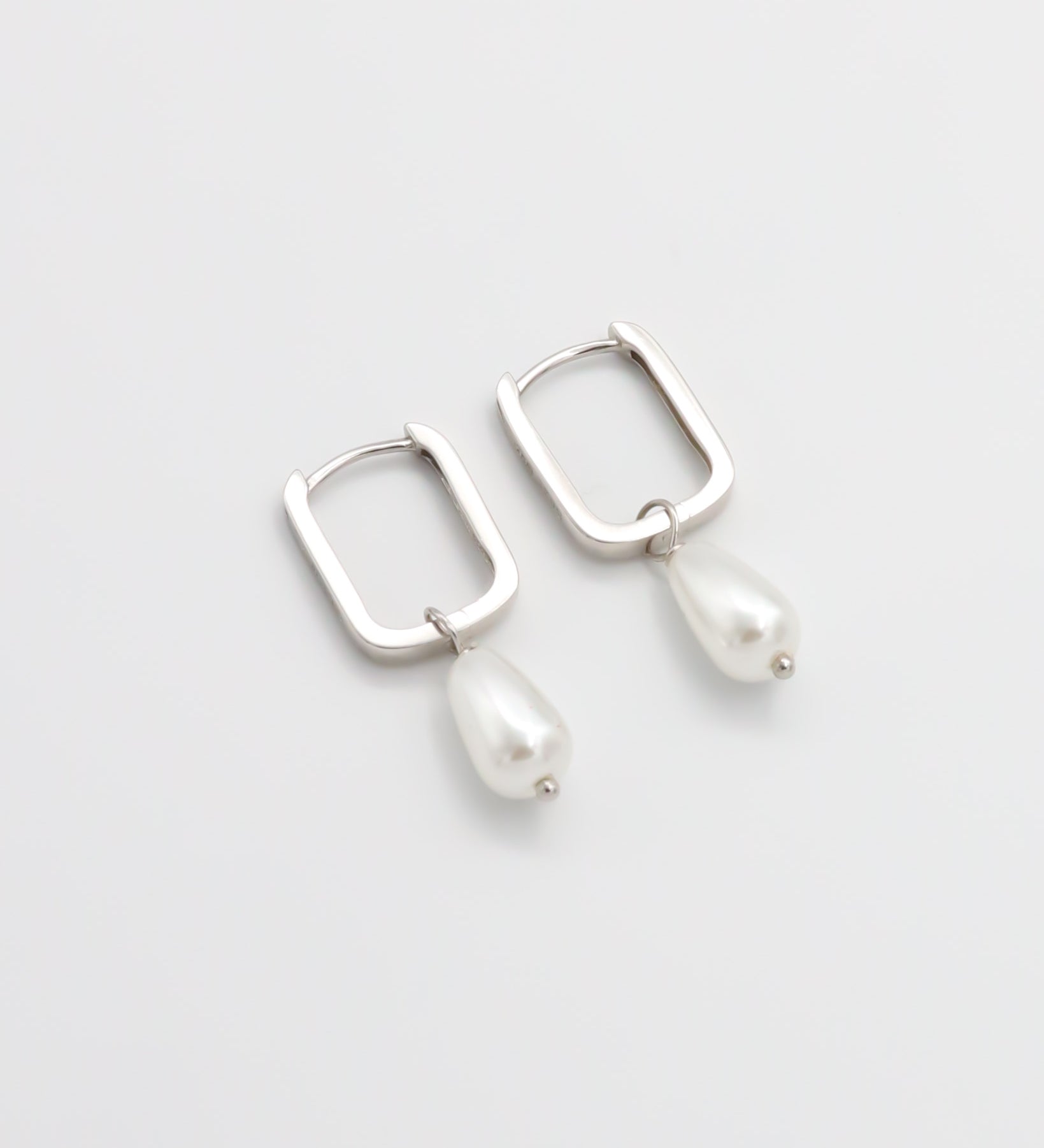 A pair of silver hoop earrings with pearl accents on a white background
