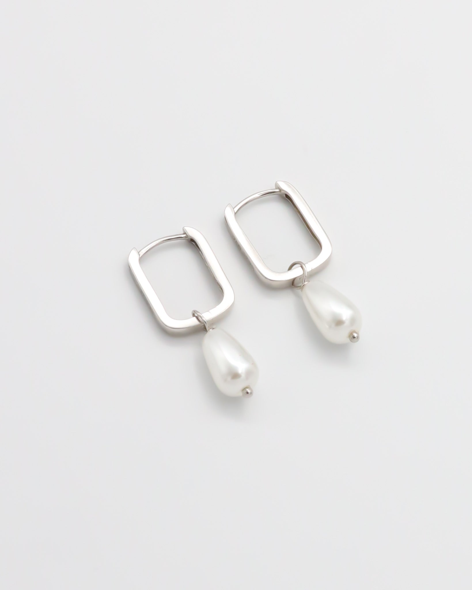 A pair of silver hoop earrings with pearl accents on a white background