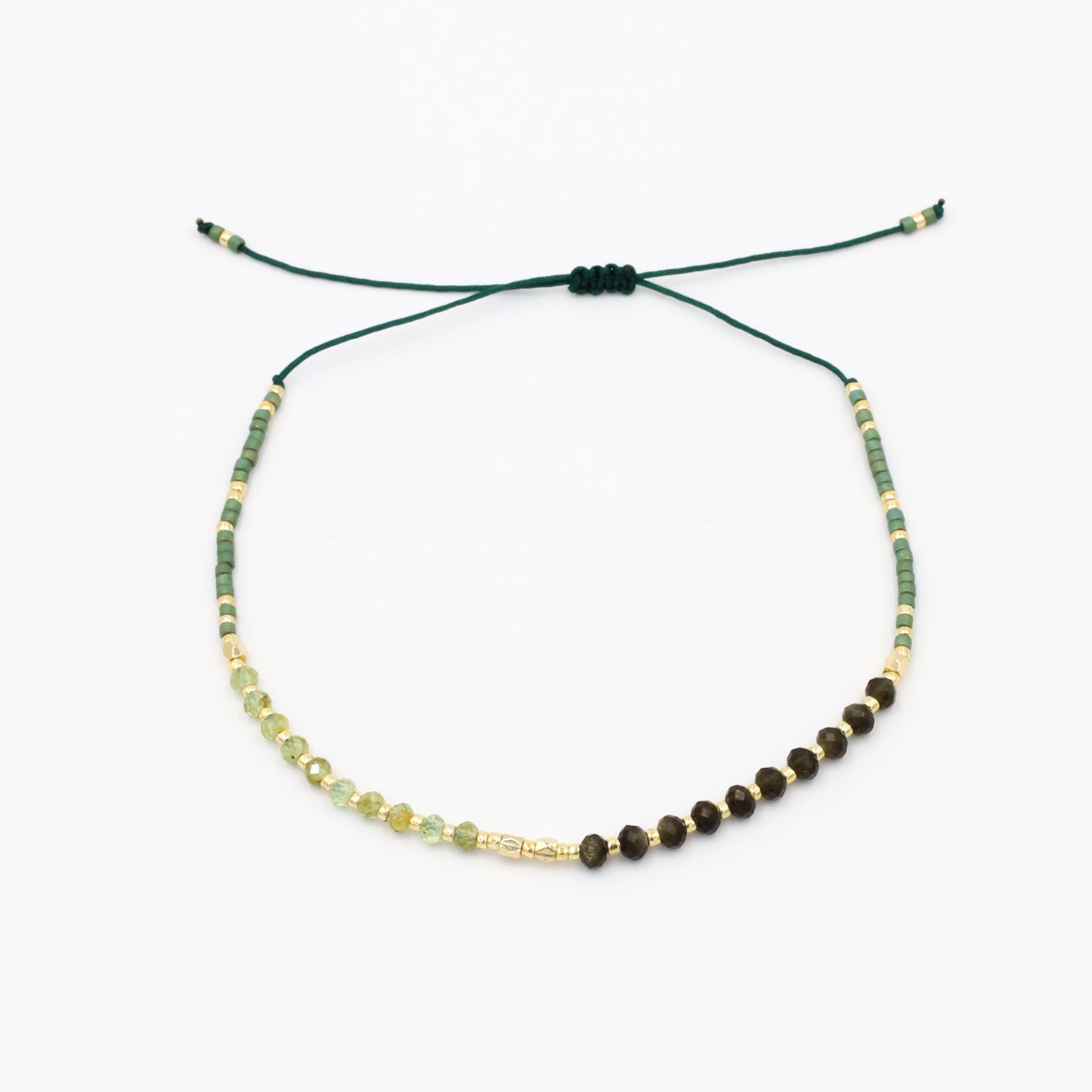 A beaded bracelet with a mix of green, gold, and brown colors, featuring rhinestones and an adjustable cord.