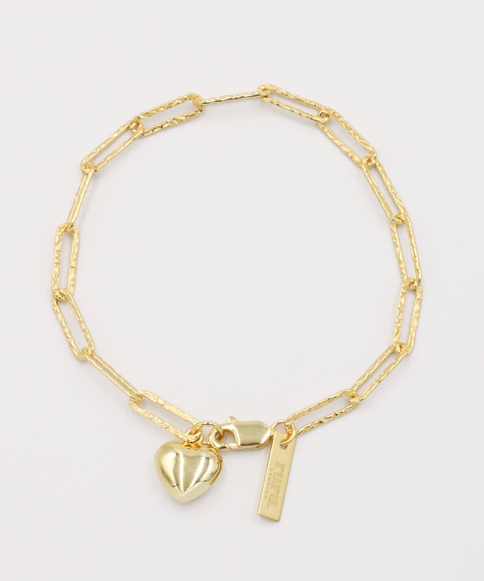 A gold-colored bracelet with a heart-shaped charm and a small tag on a white background.