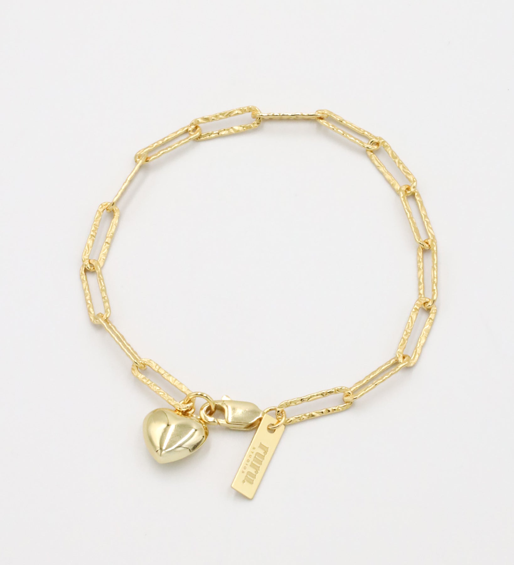A gold-colored bracelet with a heart-shaped charm and a small tag on a white background.