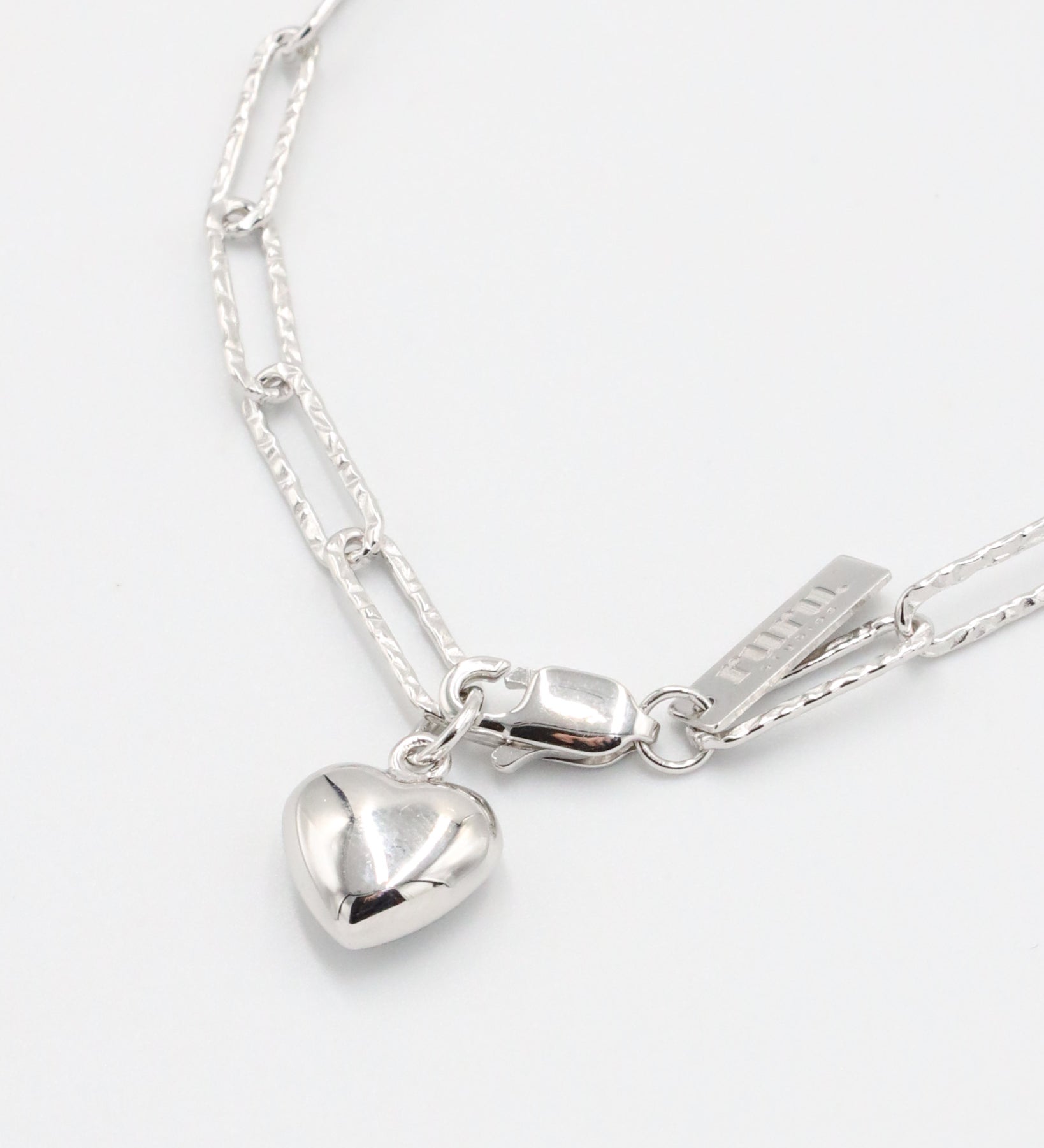 A silver bracelet with a heart-shaped charm on a white background - Close Up.