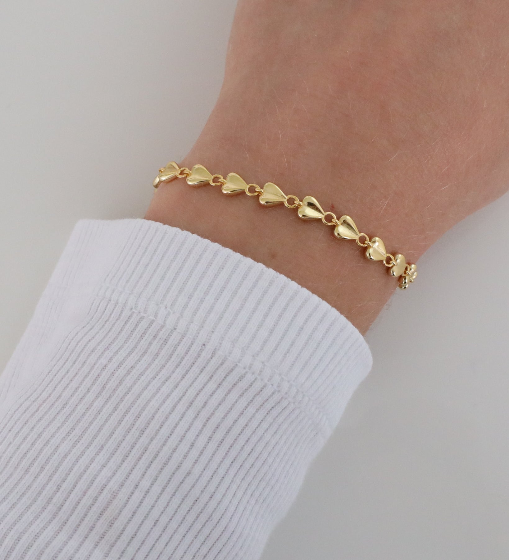 Close-up of a wrist wearing the delicate Josie bracelet with heart-shaped elements and a polished finish, styled with a white ribbed long sleeve.