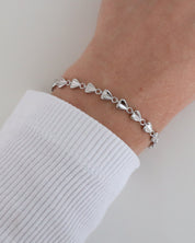 Close-up of a wrist wearing the delicate Josie bracelet with heart-shaped elements and a polished finish, styled with a white ribbed long sleeve.