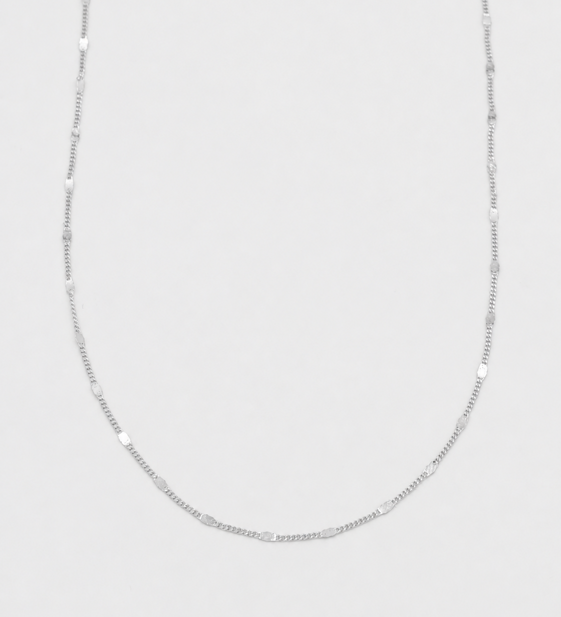 A delicate silver chain necklace with alternating smooth oval beads and small spacer rings, displayed against a light gray background.