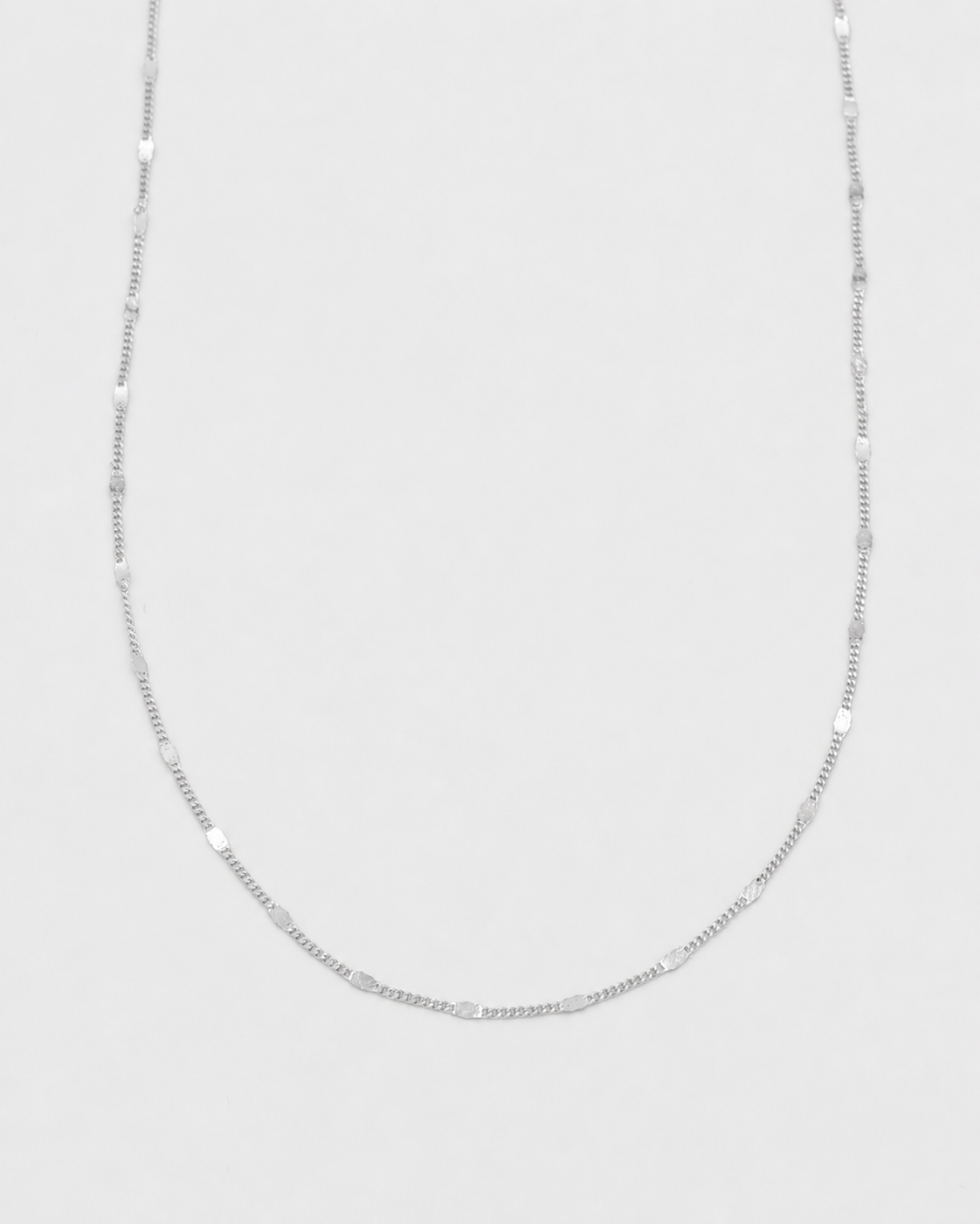 A delicate silver chain necklace with alternating smooth oval beads and small spacer rings, displayed against a light gray background.