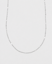 A delicate silver chain necklace with alternating smooth oval beads and small spacer rings, displayed against a light gray background.