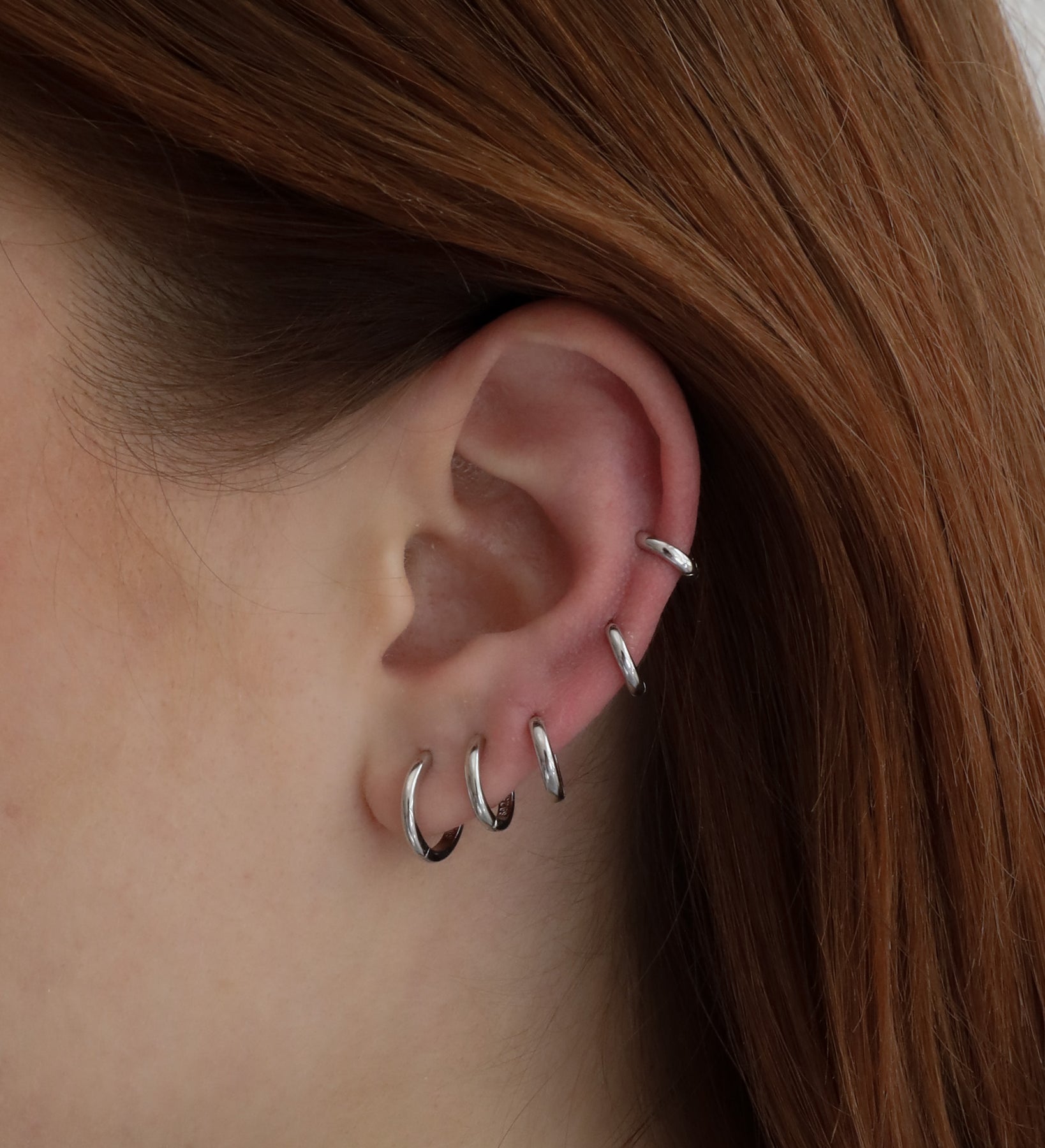 Close-up of an ear wearing six Lu Earrings in different sizes, styled across multiple piercings for a stacked and minimal look.