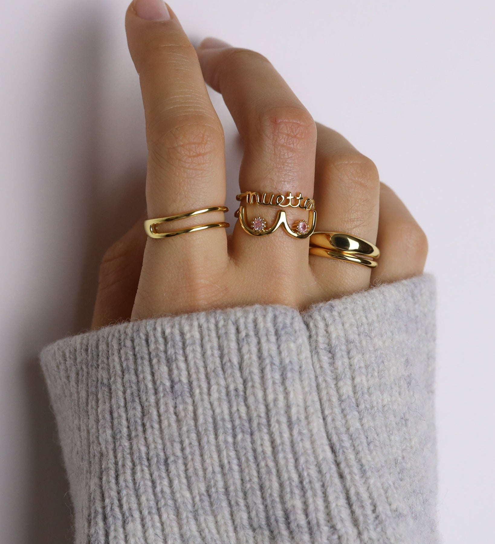 Hand wearing multiple gold rings with a neutral background