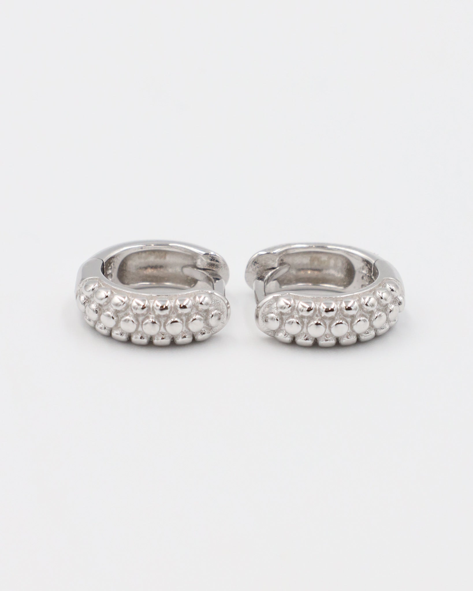 A single silver hoop earring with a pressure system anchoring and small decorative stones around the edge.