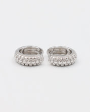 A single silver hoop earring with a pressure system anchoring and small decorative stones around the edge.
