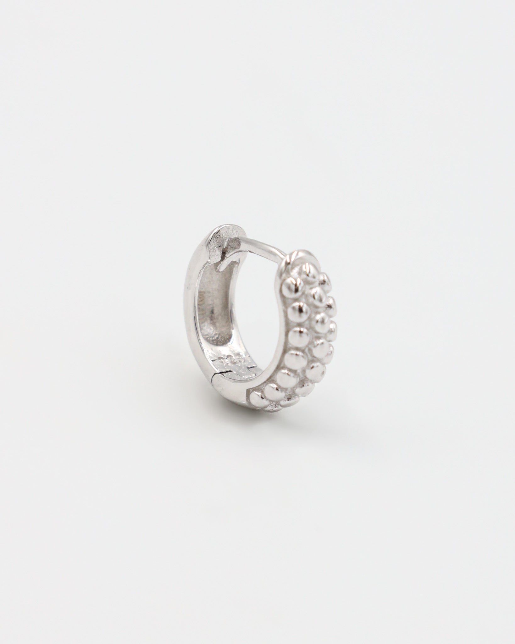 A single silver hoop earring with a pressure system anchoring and small decorative stones around the edge.