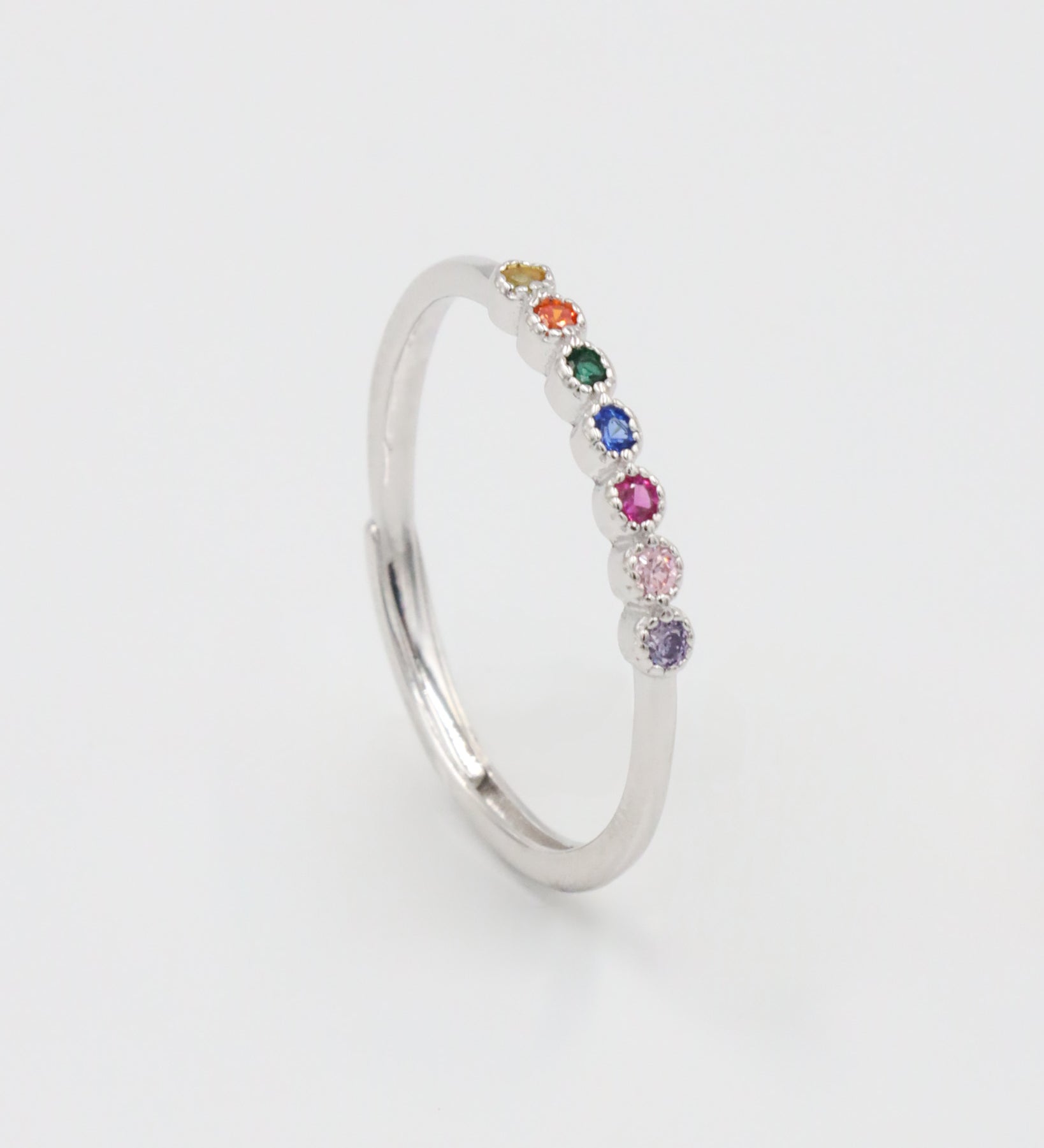 A silver ring with multiple colorful gemstones set in a line on a white background.
