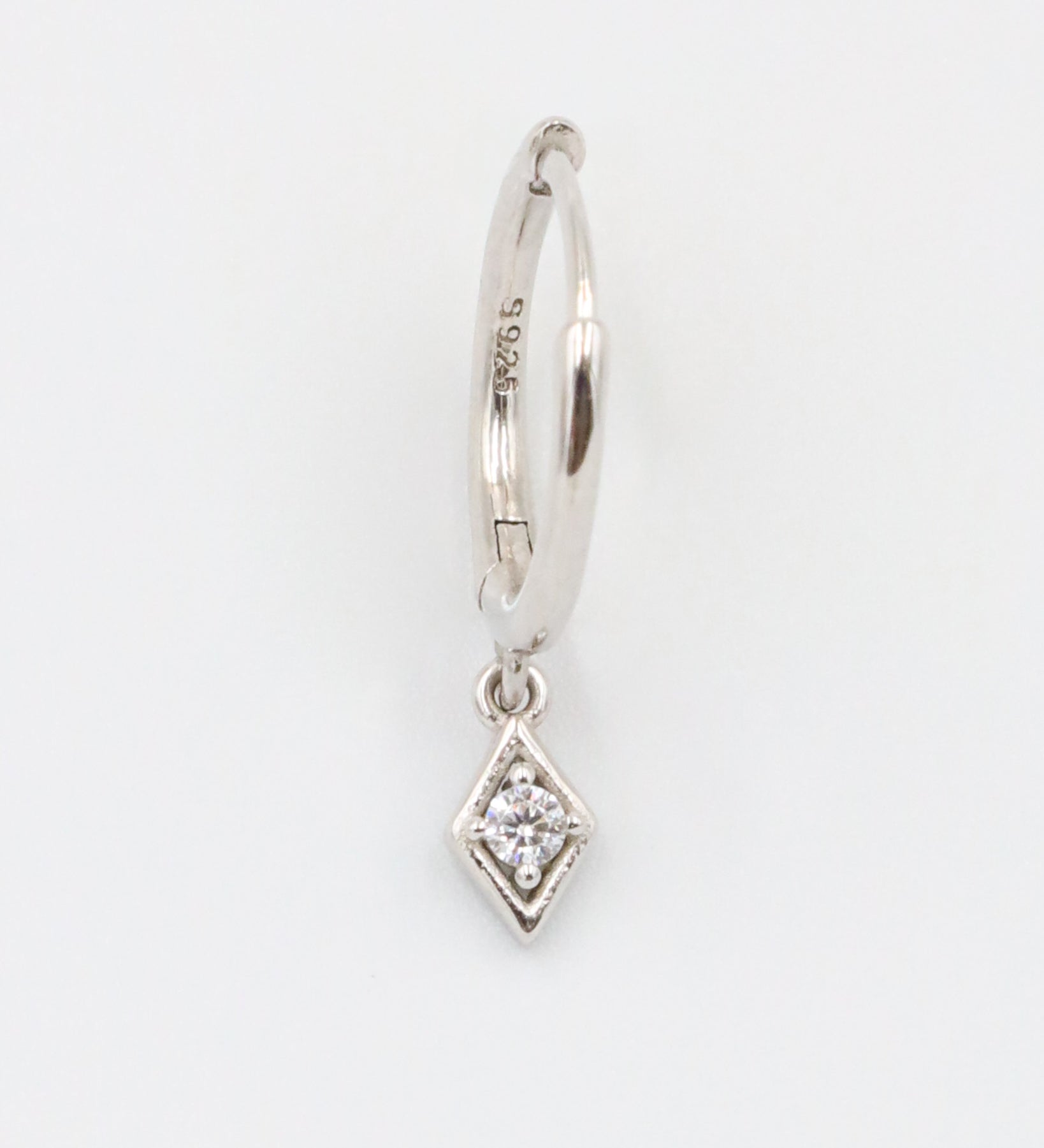 A single silver hoop earring with a small diamond-shaped pendant attached to it, displayed against a white background.
