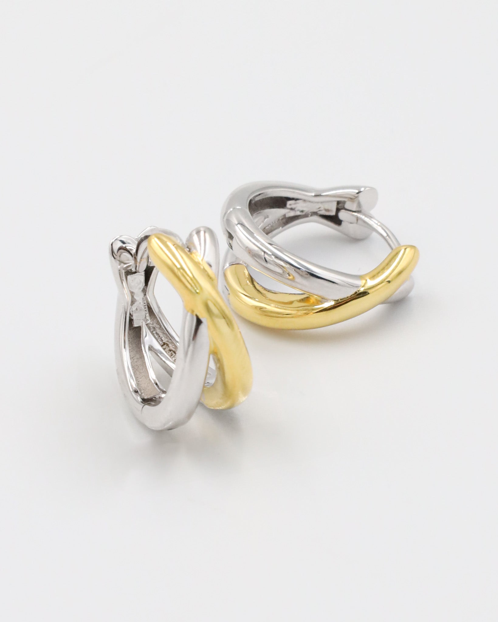 A pair of hoop earrings with one half in silver and the other half in gold color, connected by a hinged clasp.