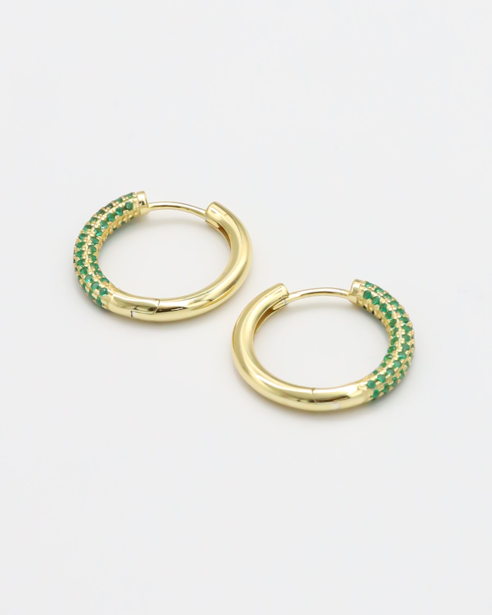 A pair of gold-colored hoop earrings with green accents, displayed against a white background.