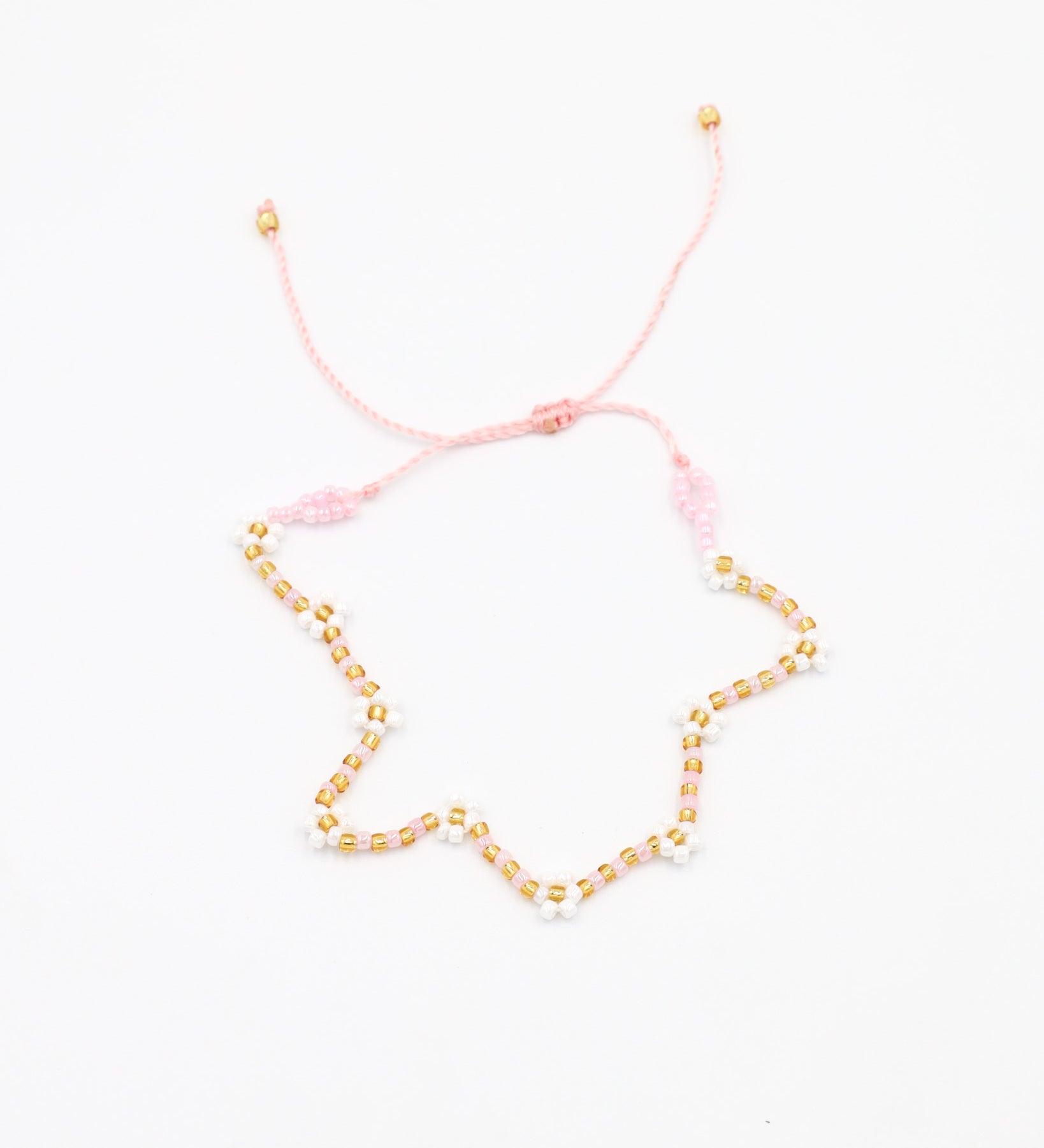 Beaded bracelet in light pink, white and gold tones with a zigzag pattern and adjustable sliding closure, laid flat on a white background.
