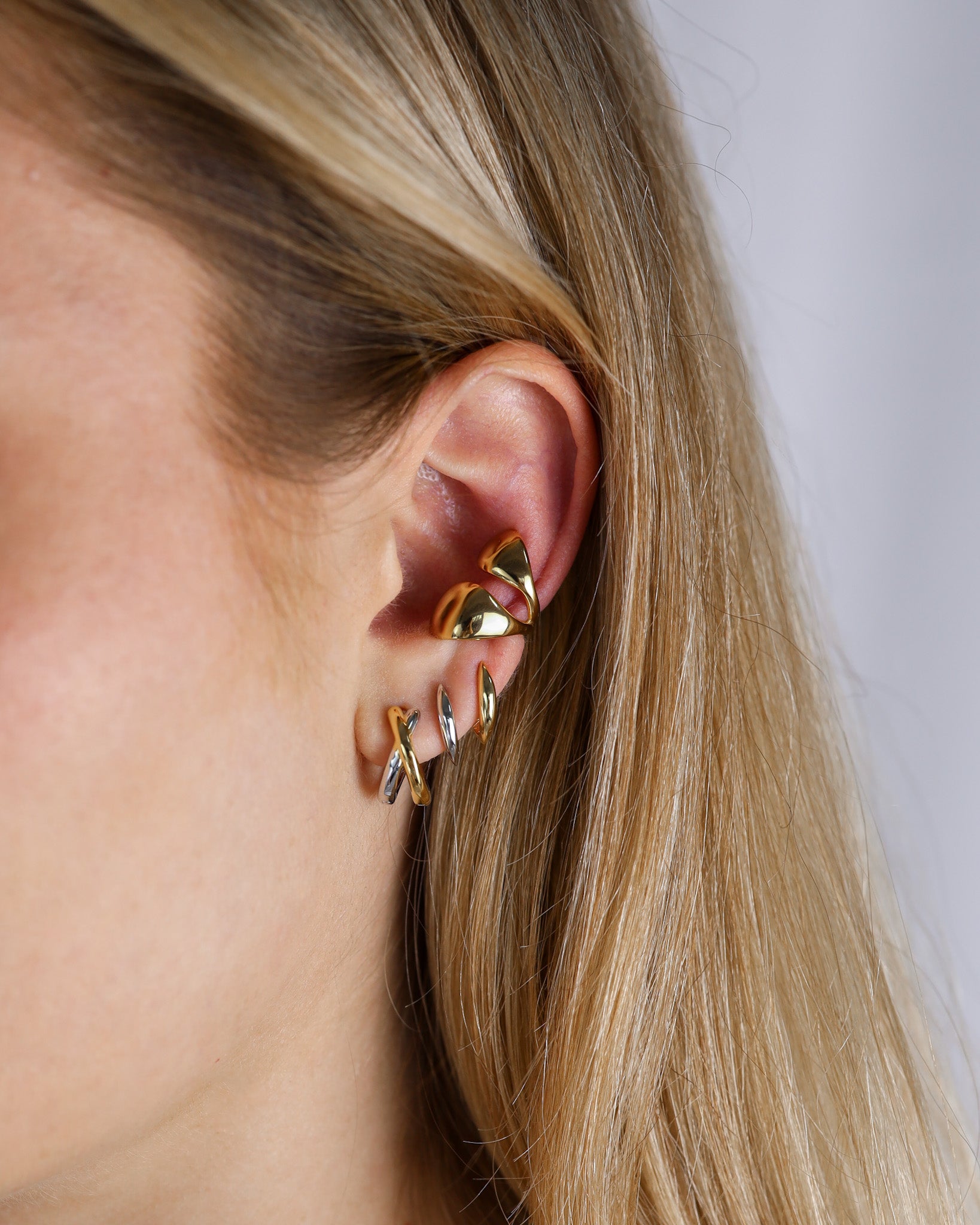 Gold earrings worn by a person with blonde hair on a neutral background