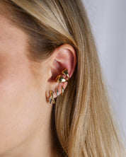 Gold earrings worn by a person with blonde hair on a neutral background