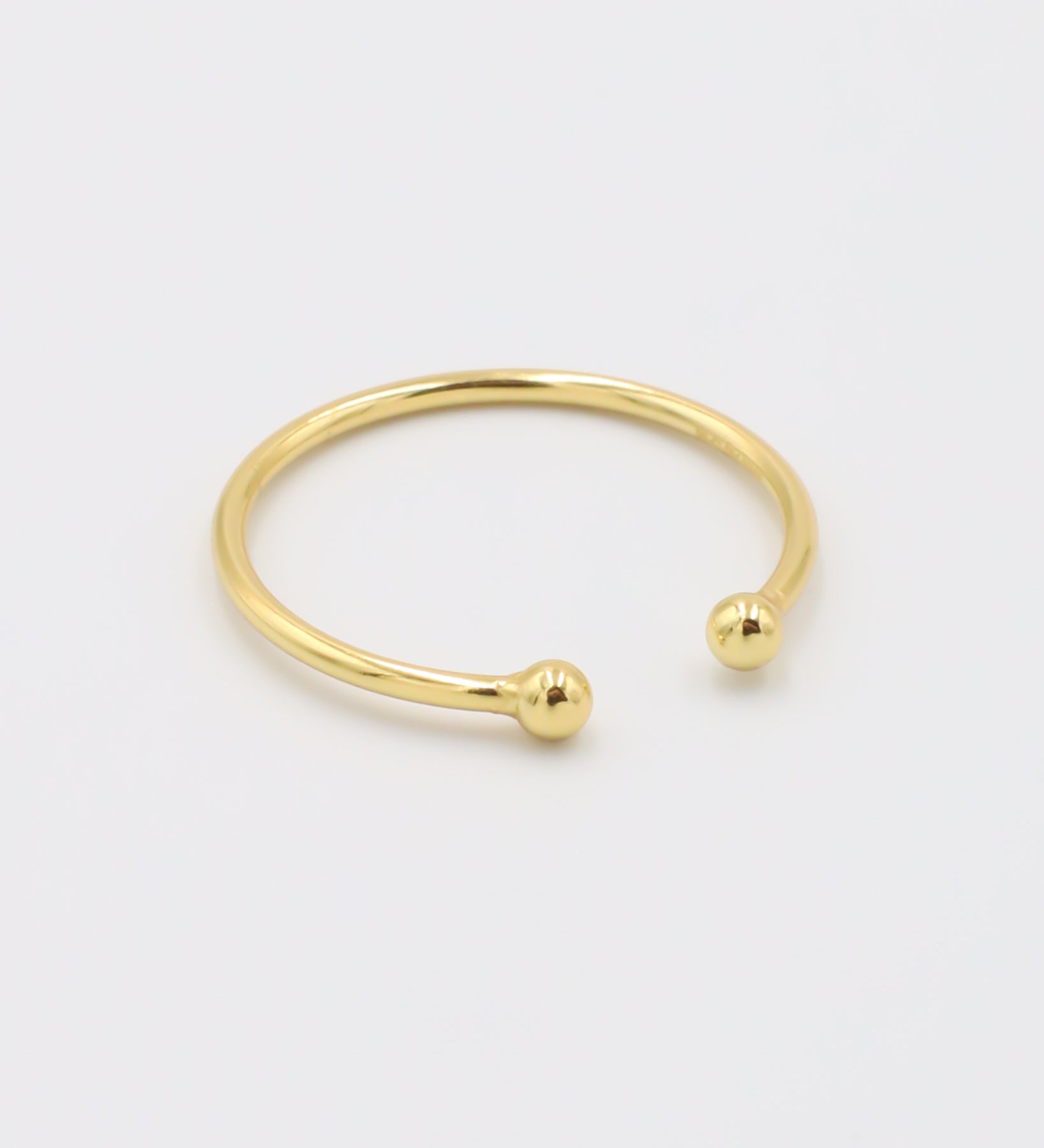 A simple gold-colored ring with two spherical decorations, displayed against a white background.