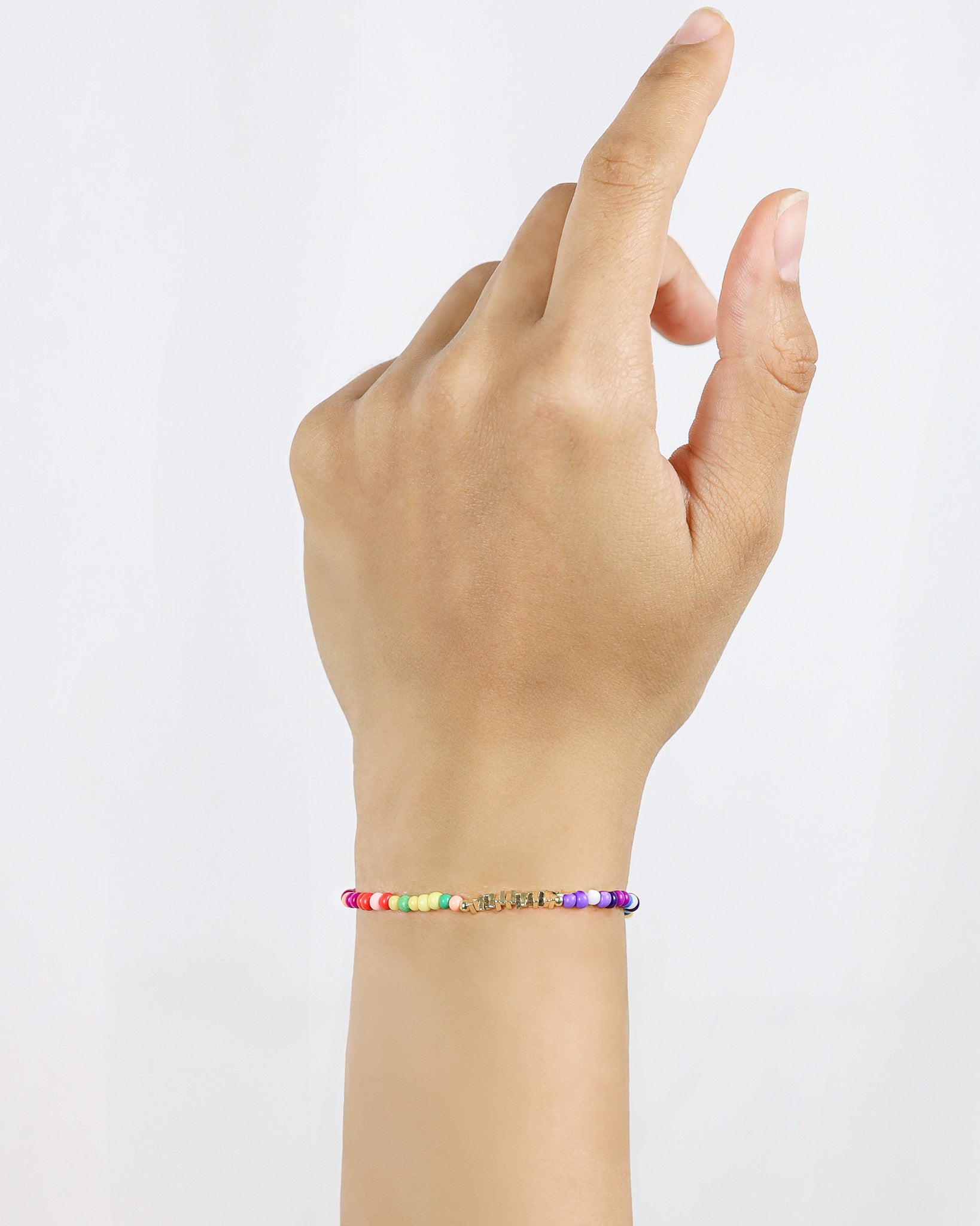 Hand wearing a colorful beaded bracelet on a plain background