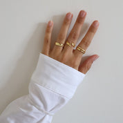 A gold-colored ring with intricate designs worn by a hand against a white background.