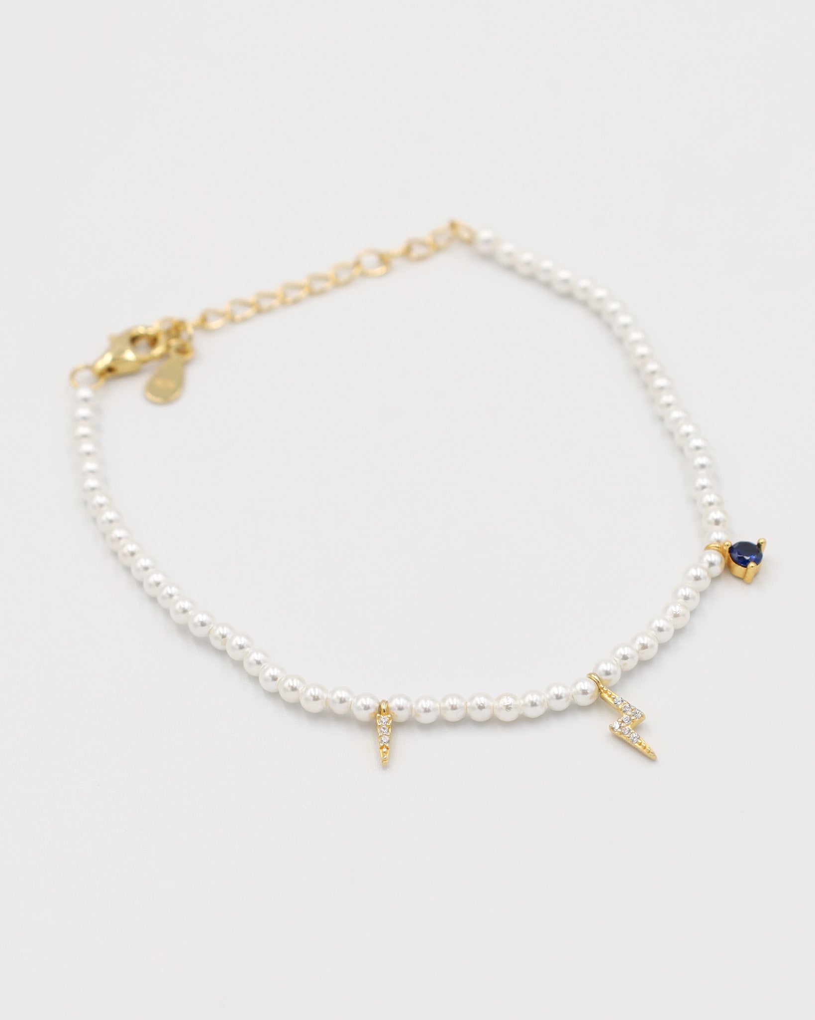 A gold-colored bracelet featuring white pearl beads and small gold charms, including a key-shaped charm.