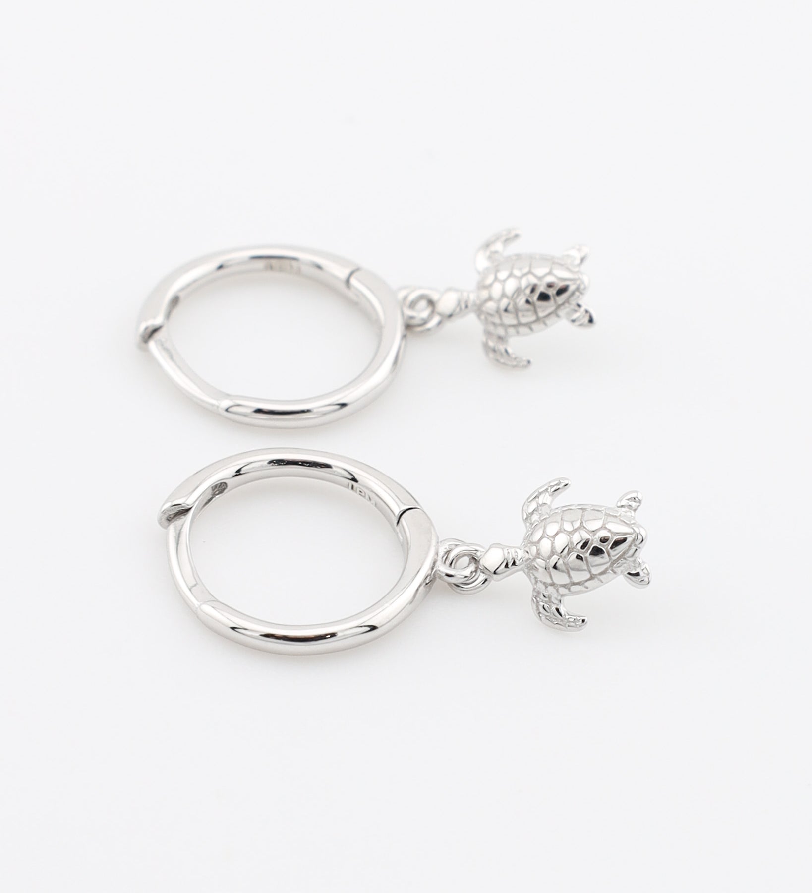 Two silver hoop earrings with turtle charms on a white background