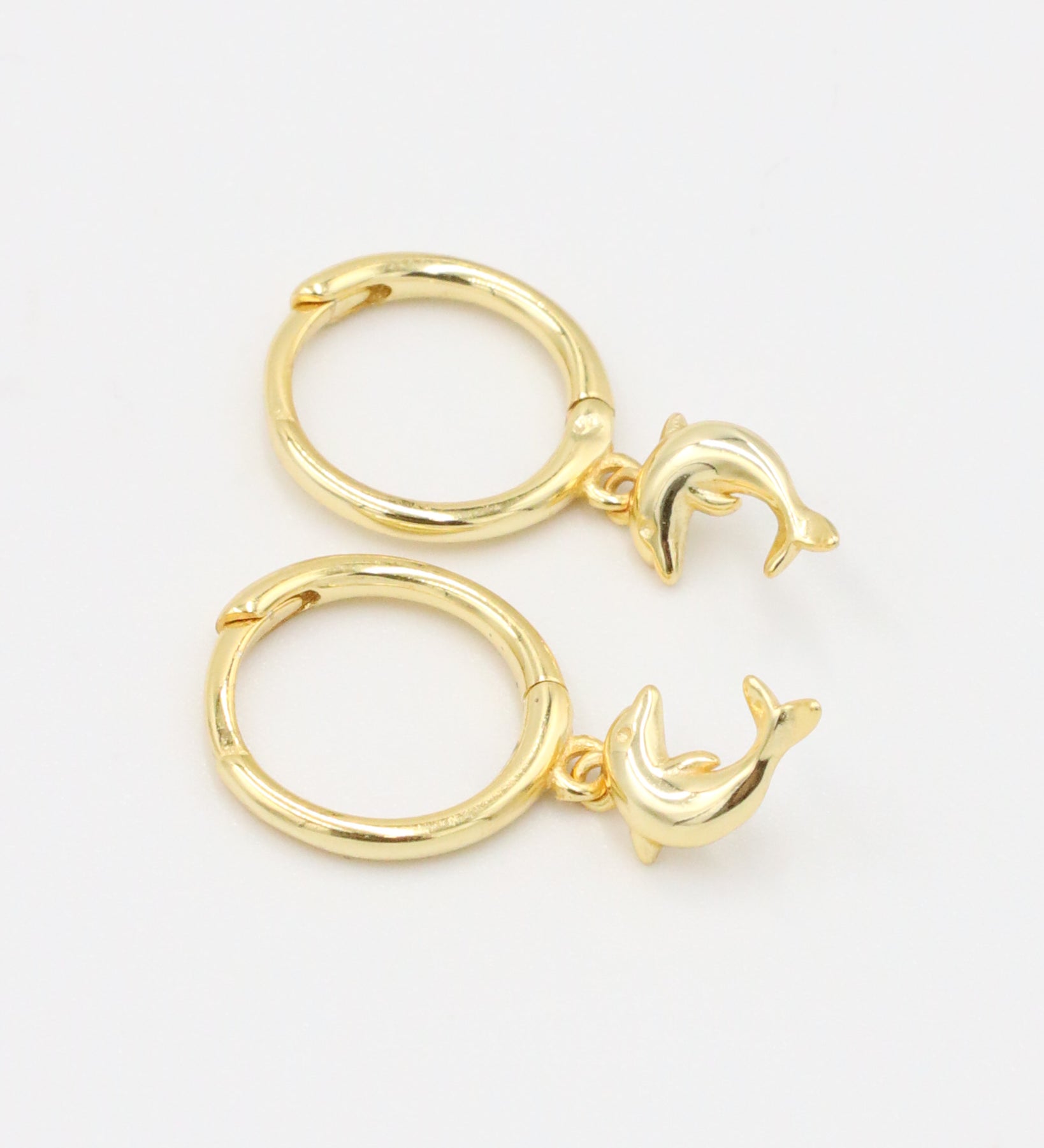 Pair of gold-plated sterling silver hoop earrings with dolphin charms, side view.
