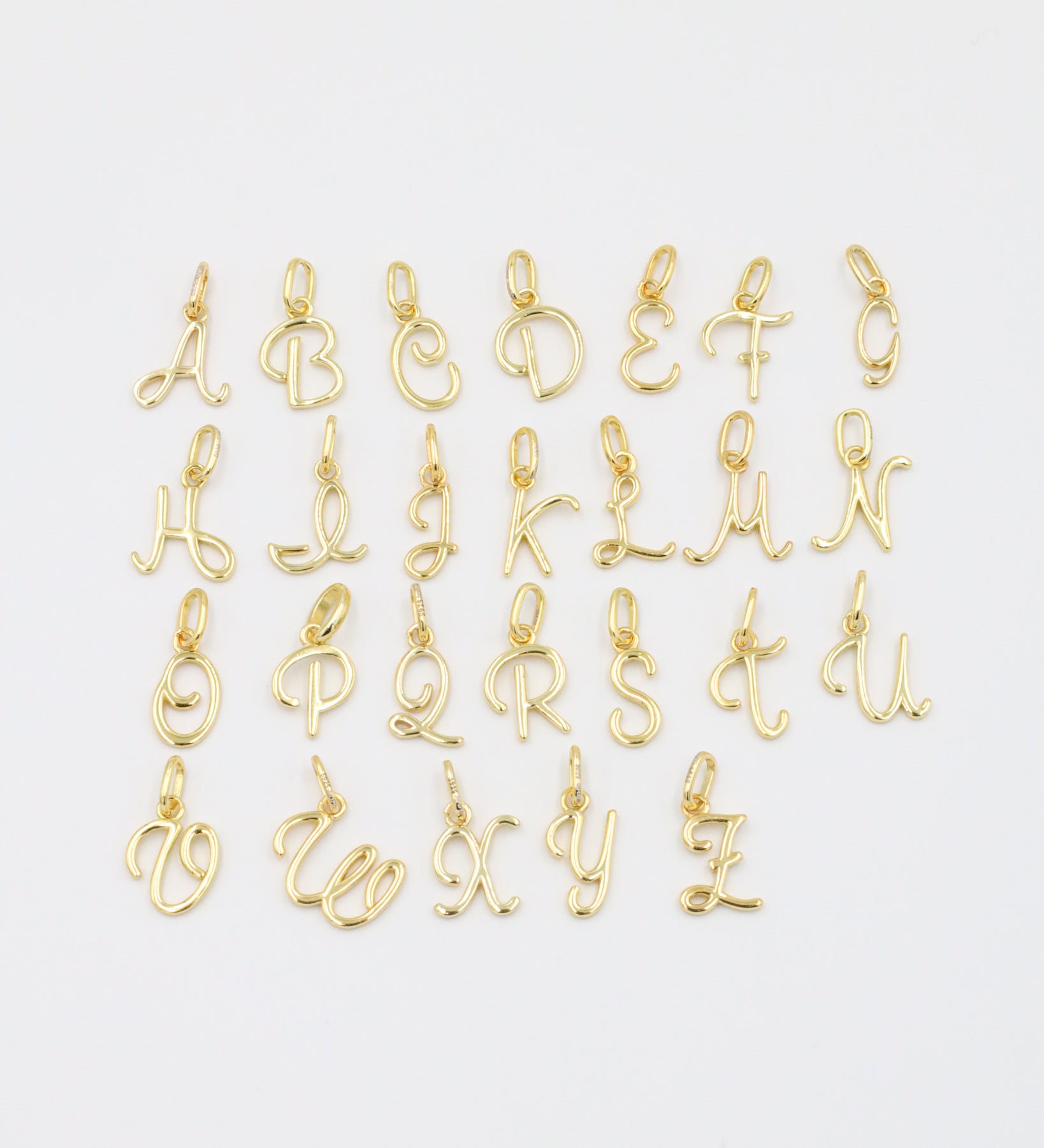 A set of gold-plated letter curve alphabet pendants spread flat in a display.