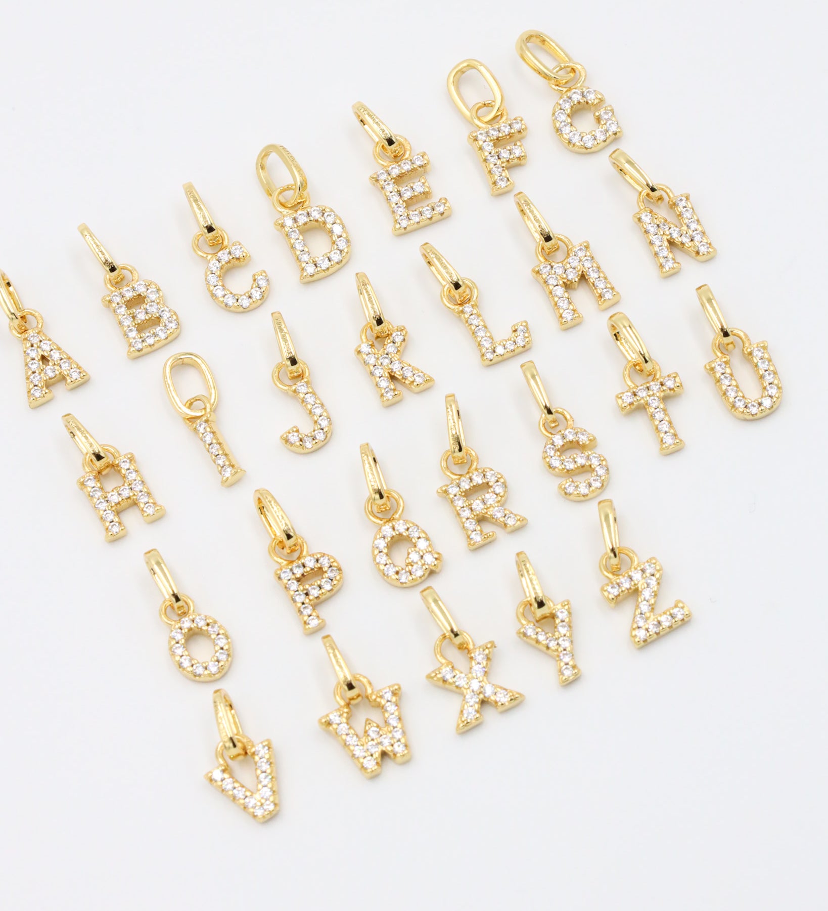 Gold-plated letter pendants in an A-Z arrangement, captured at an angle to highlight their sparkling zirconia stones.