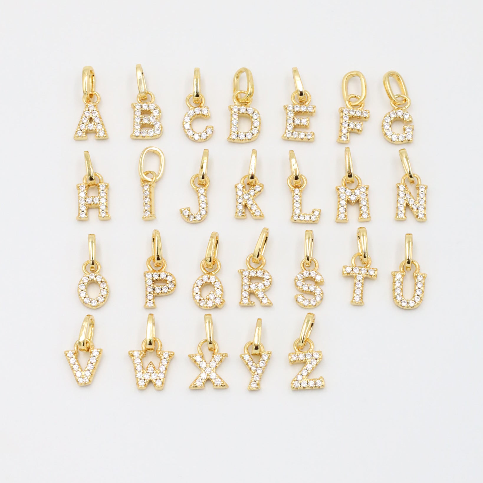 Gold-plated sparkly letter pendants arranged in a complete A-Z display, showcasing their zirconia embellishments.