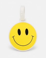 Smiley suitcase tag by ruru. studios with a yellow smiley face and white loop on a clean white background